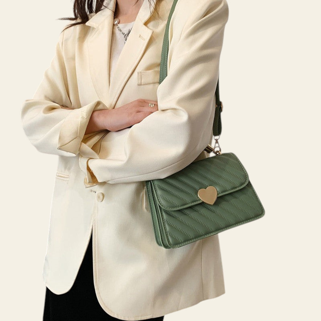 Person wearing a cream blazer holding a green handbag with a heart emblem.