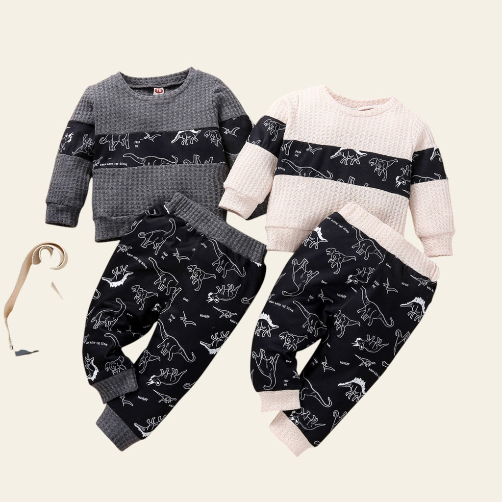 Two children's outfits with dinosaur patterns on a wooden surface.
