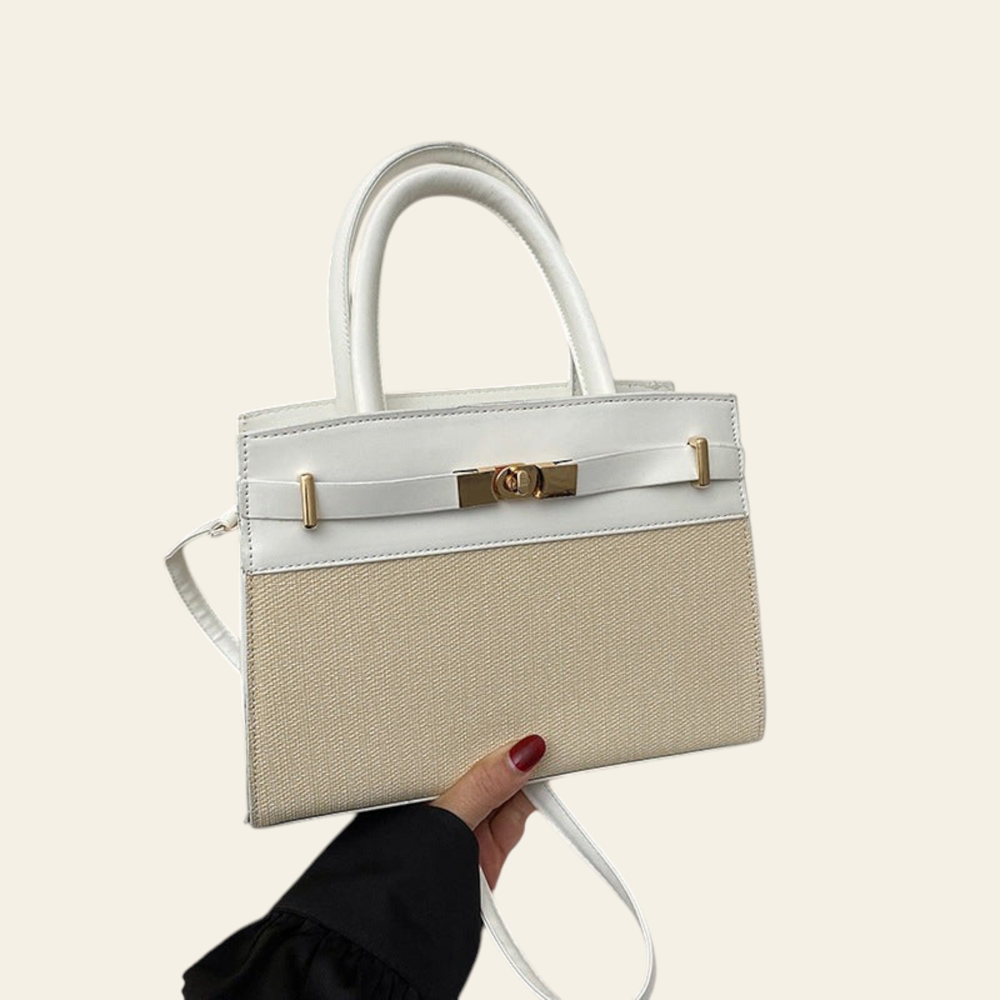 Handbag with white top handle and beige body held by a hand on a light surface.
