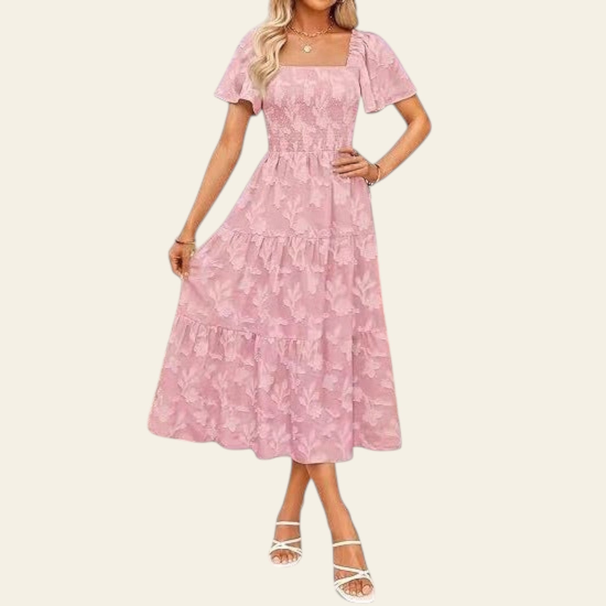 Woman wearing a pink floral dress standing outdoors with a geometric wall and plants in the background.