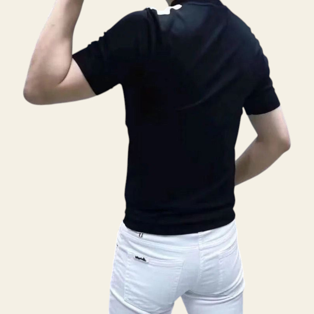 Man wearing a black short sleeve t-shirt with white pants, standing in front of a marble wall