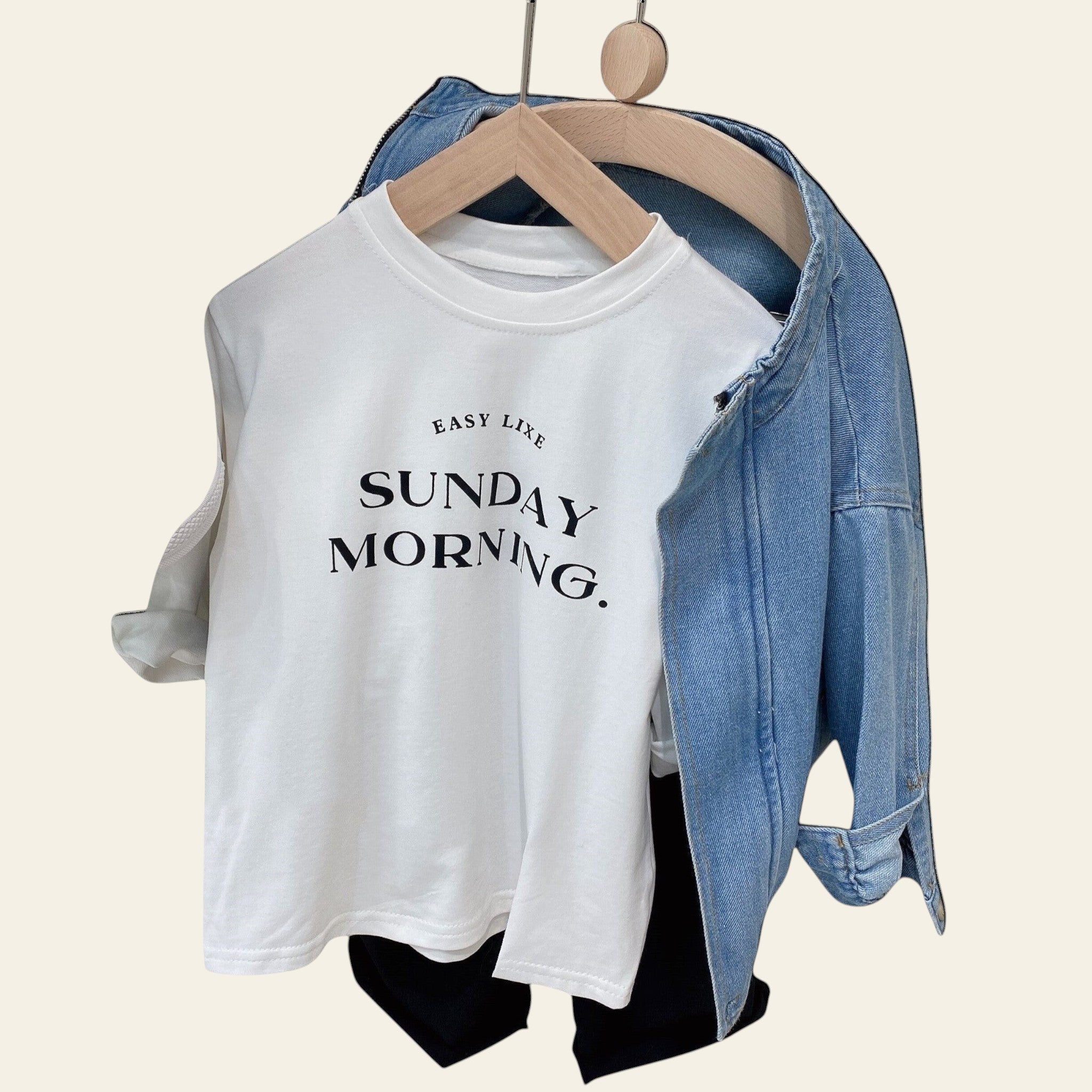 White t-shirt with 'Easy Life Sunday Morning' text on a hanger with denim jacket and sneakers.