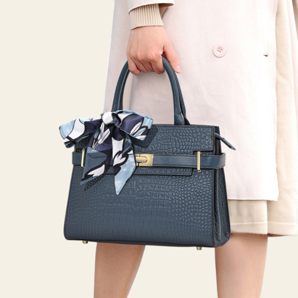 Blue handbag with a decorative bow held by a person wearing a beige coat.