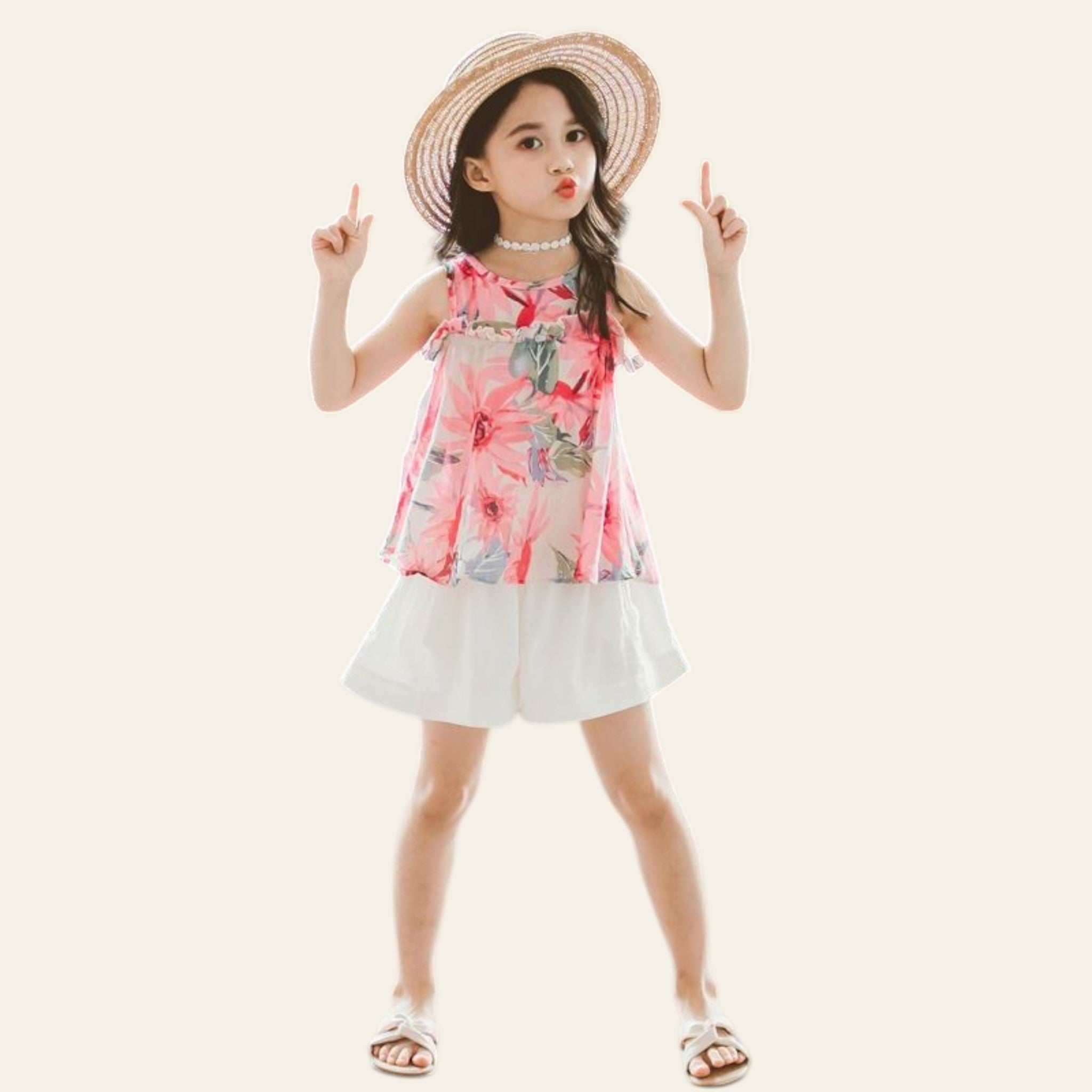 Young girl in a floral dress and straw hat posing with peace signs against a textured wall.