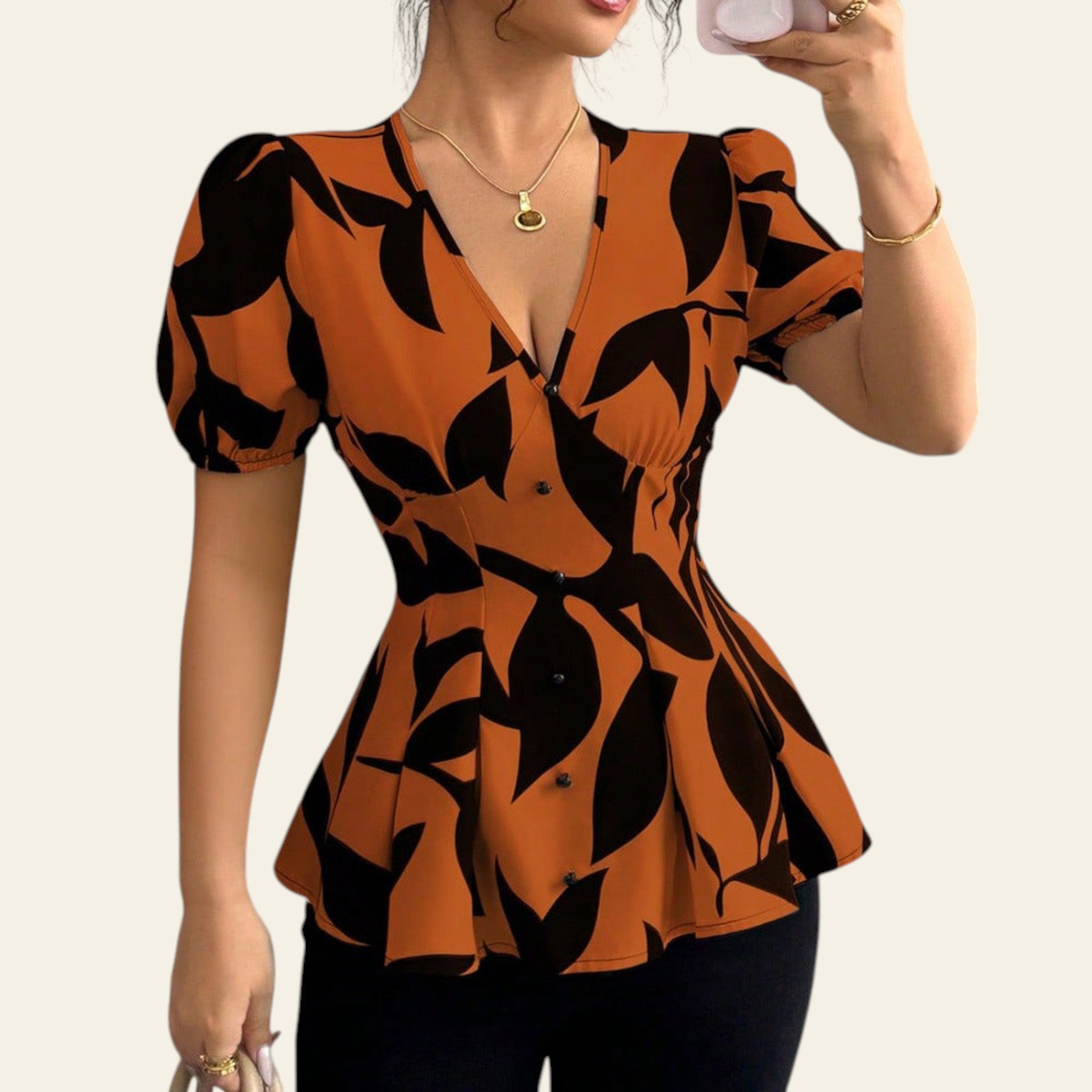 Woman wearing an orange and black patterned top taking a mirror selfie.