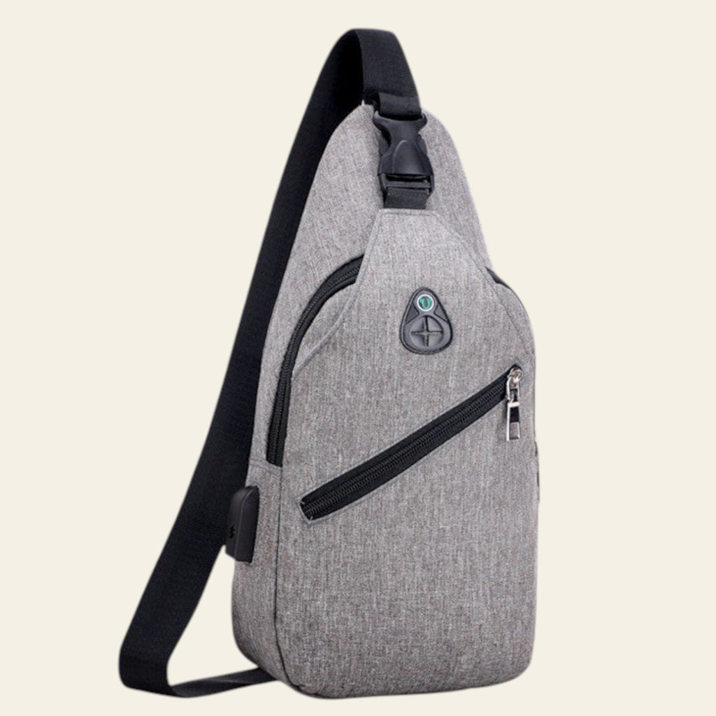 Gray sling bag with black straps against a blurred natural background