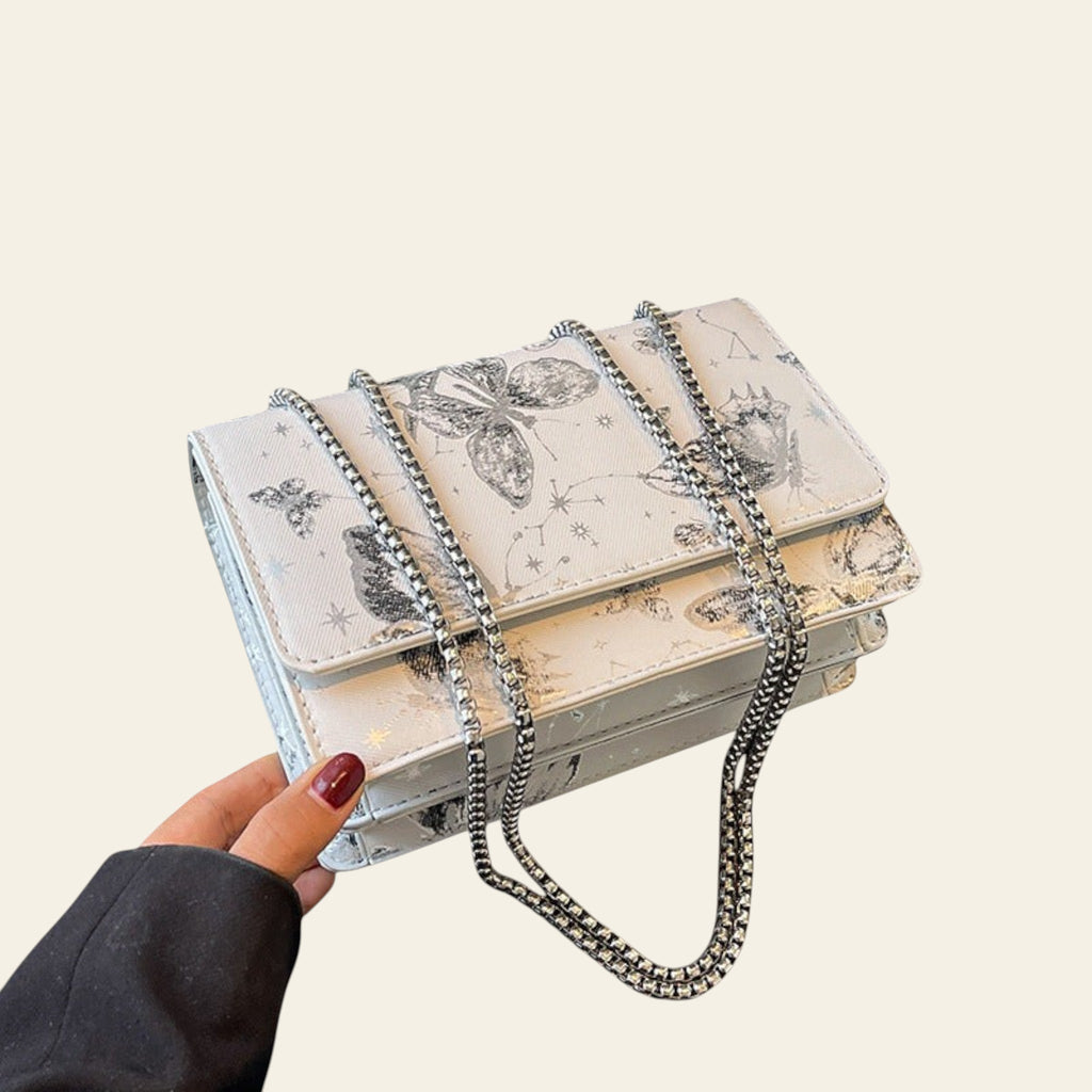 Handbag with floral design and chain strap held by a hand on a surface.
