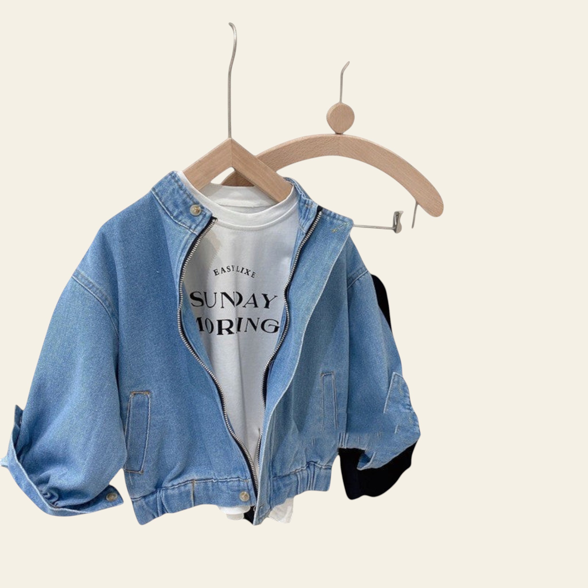 Denim jacket, white t-shirt with text, black pants, and cap on a rack against a neutral wall.