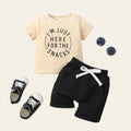 Children's outfit with t-shirt, shorts, shoes, and sunglasses on a light wooden surface.