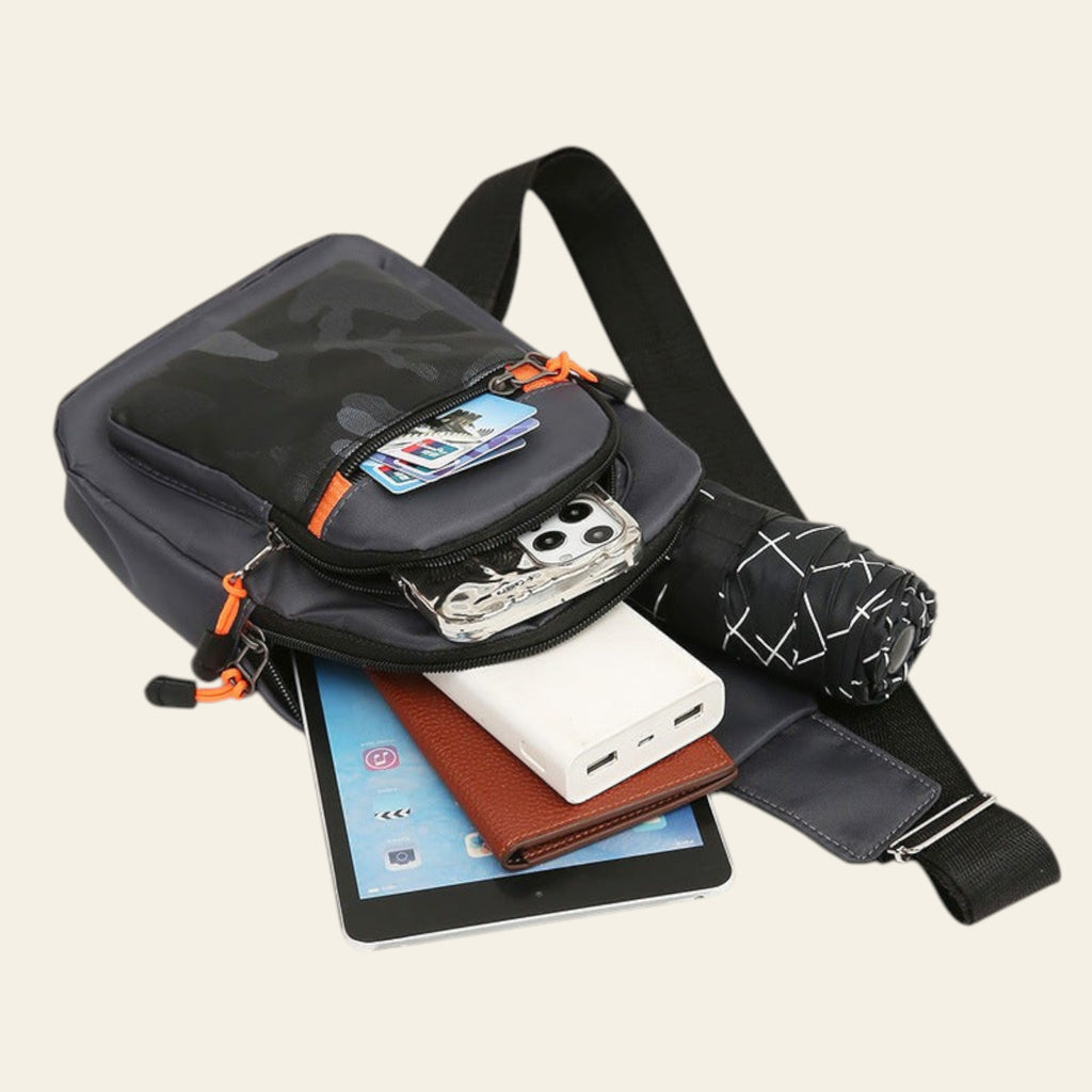 Black crossbody bag with various items including a tablet, phone, and wallet on a white background