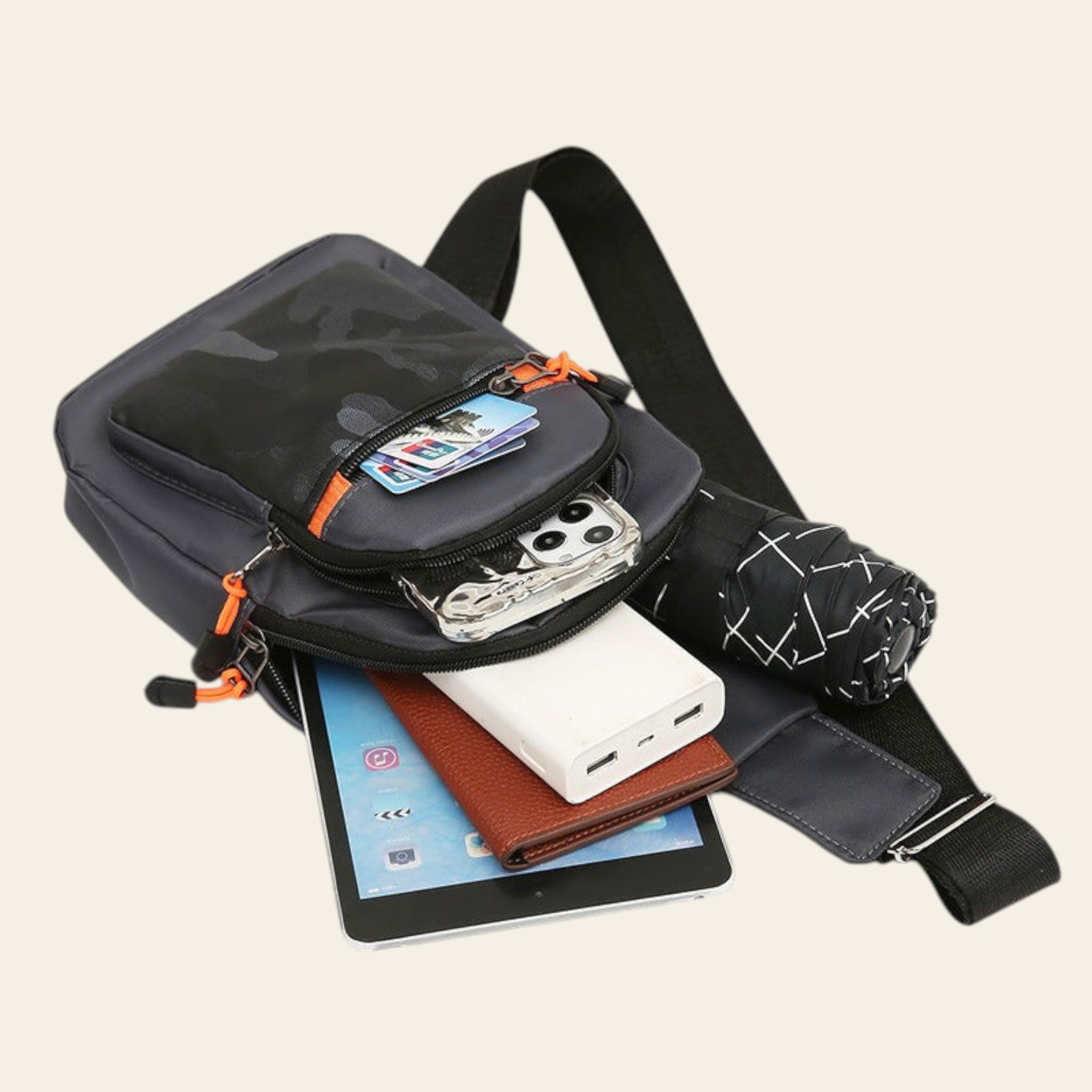 Black crossbody bag with various items including a tablet, phone, and wallet on a white background