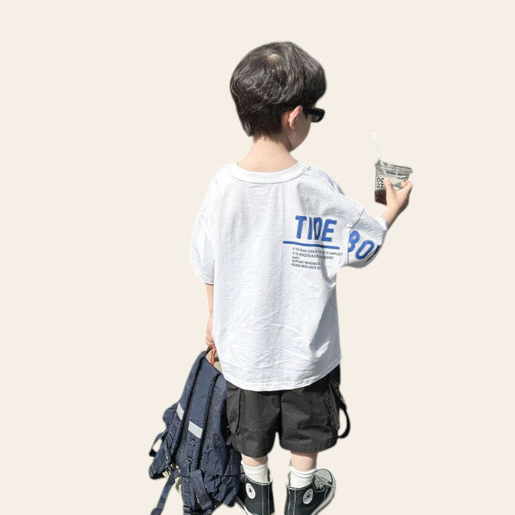 Child in a white t-shirt with blue text standing next to an open car trunk.