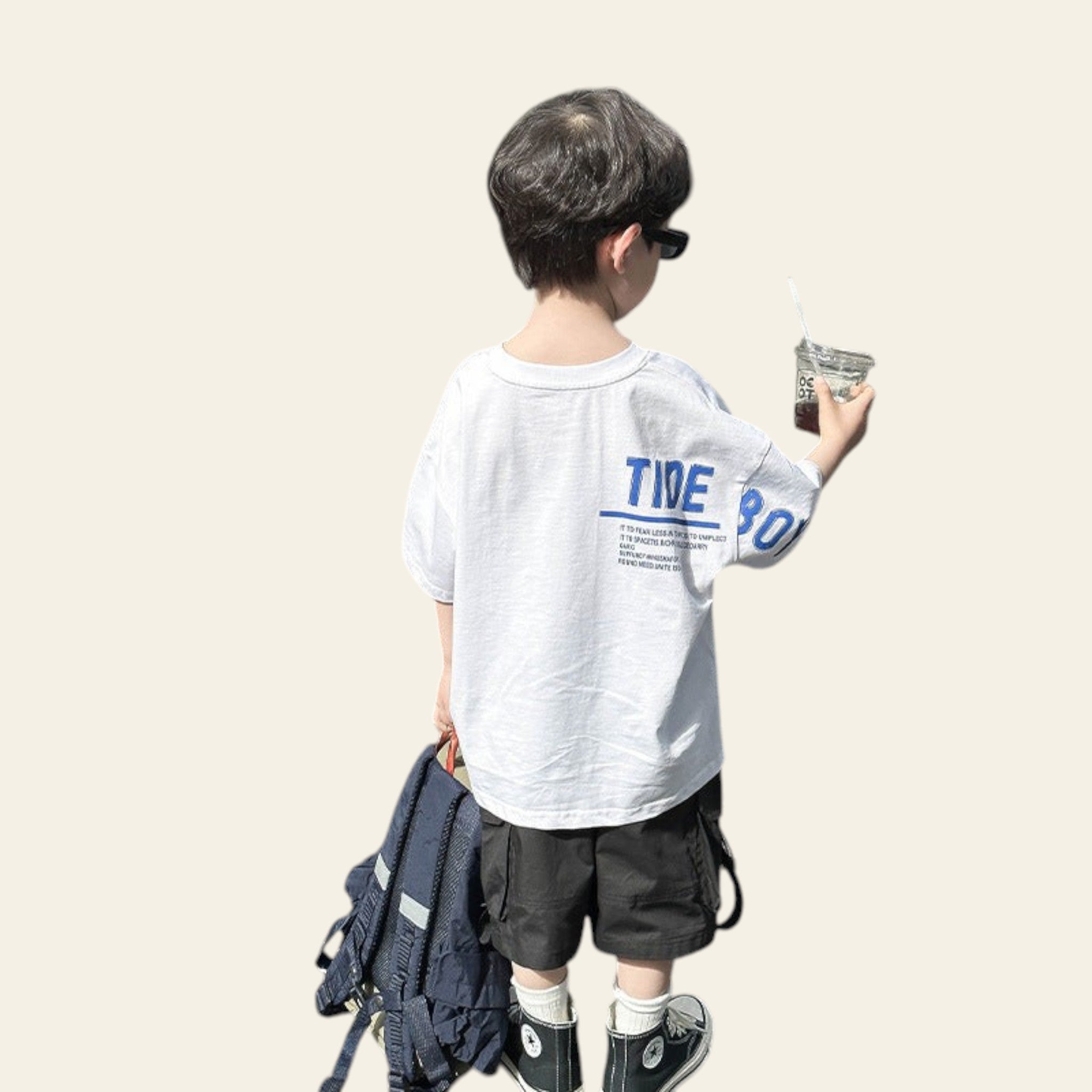 Child in a white t-shirt with blue text standing next to an open car trunk.