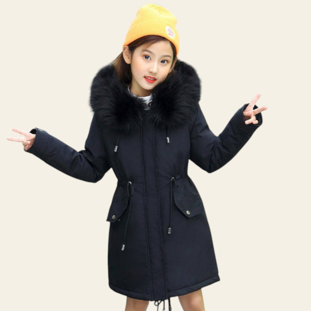 Person wearing a black coat with a large fur collar on a street.