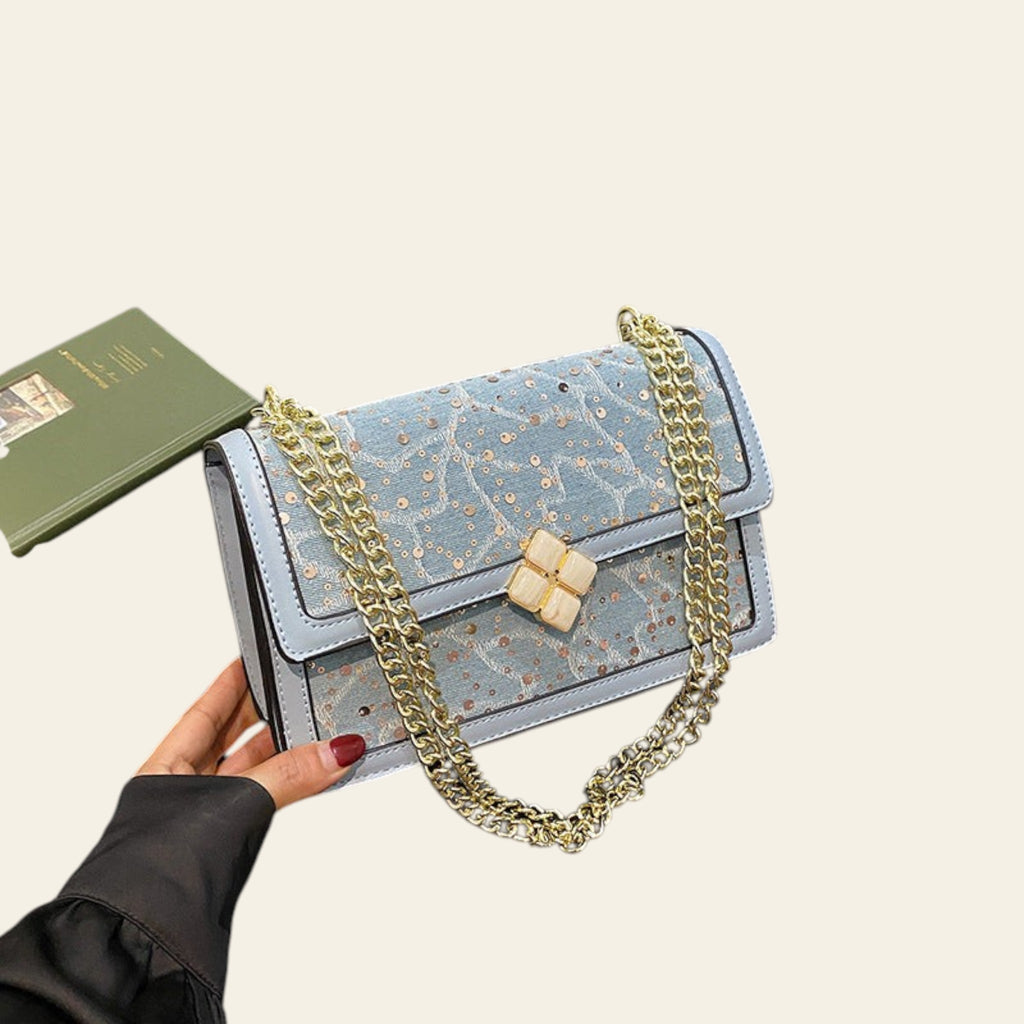 Blue handbag with gold chain on a black jacket on a wooden floor
