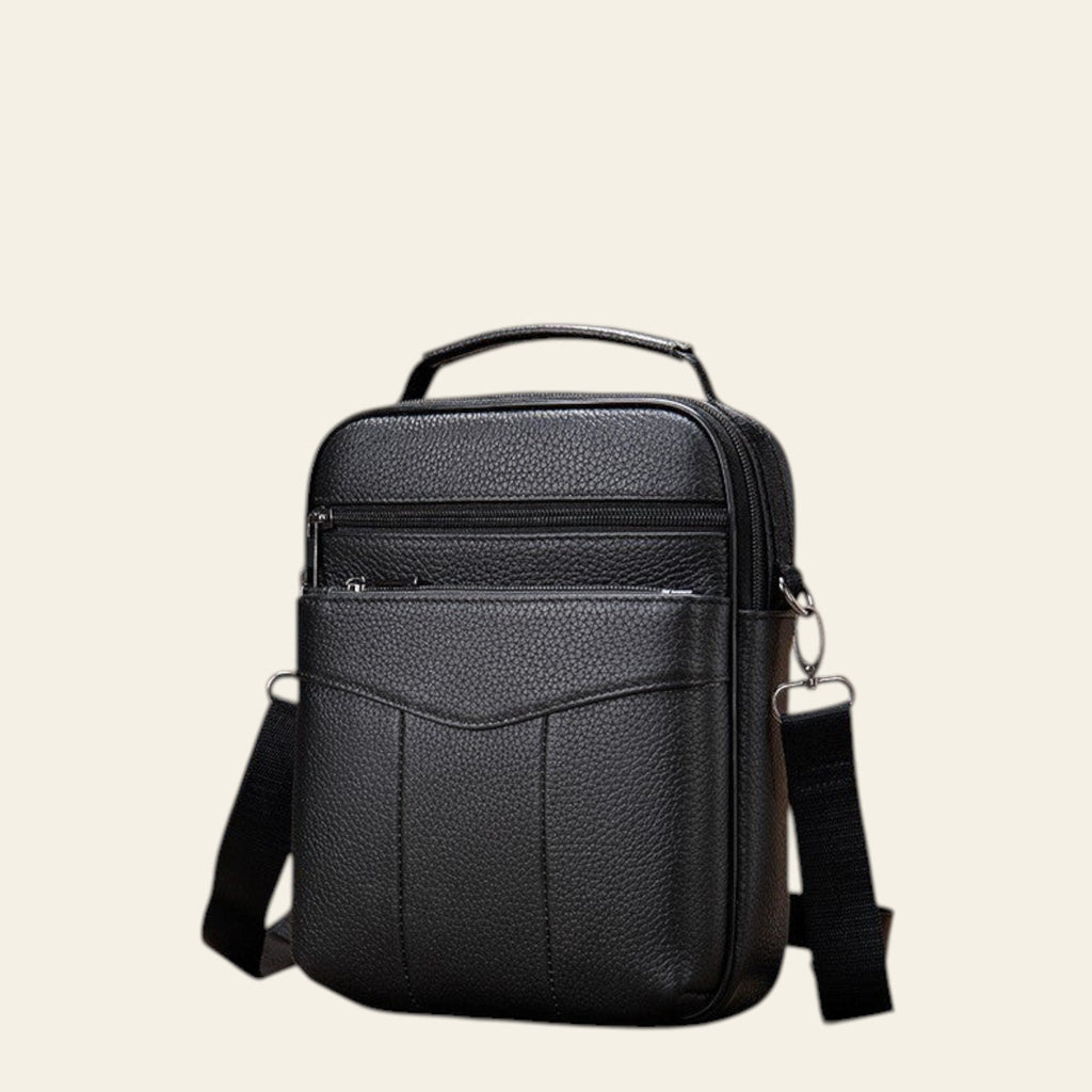 Black leather crossbody bag on a wooden floor with wooden crates and rope in the background