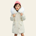Child wearing a white coat with fur hood and pink beanie on a street.