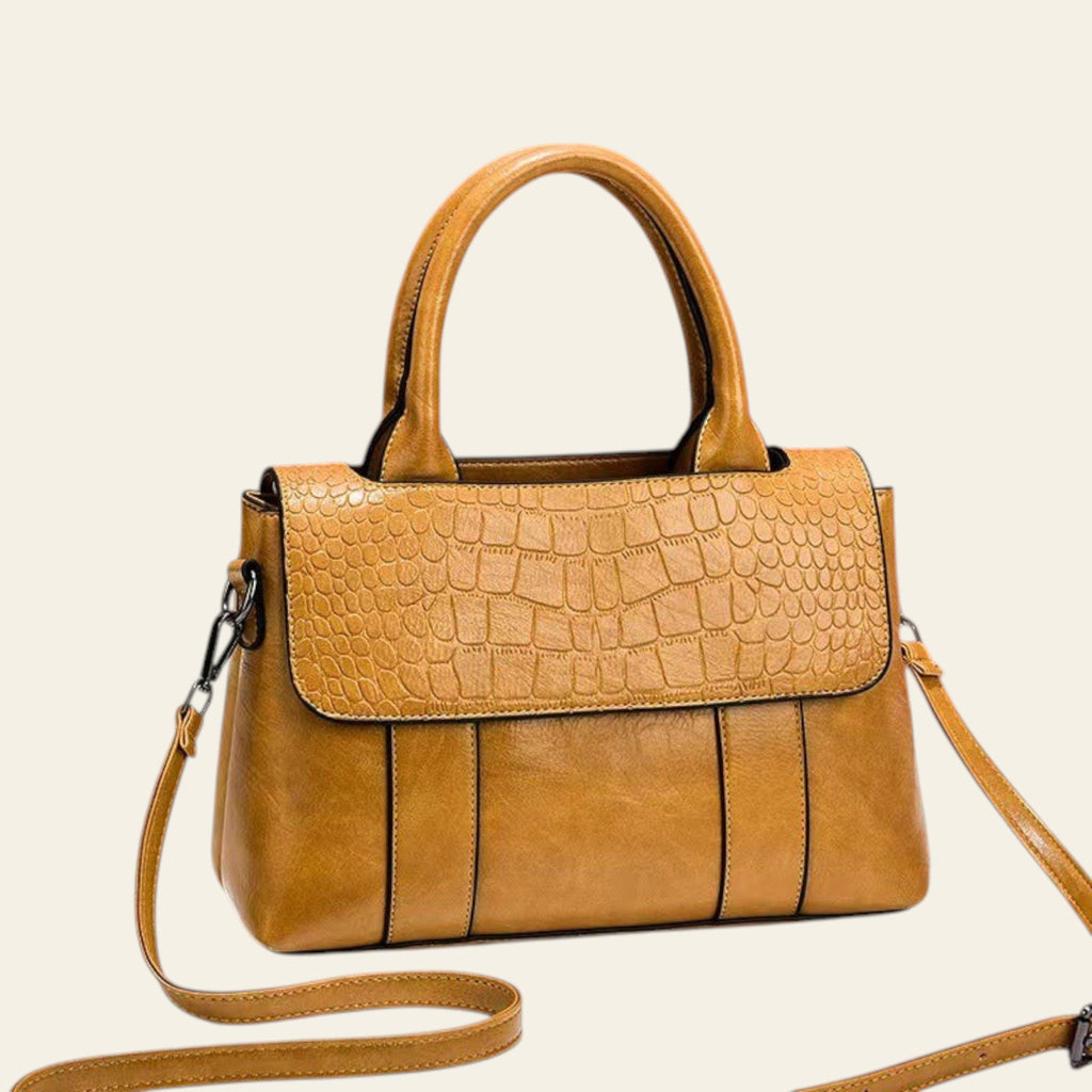 Brown handbag with crocodile texture on a white surface and brown background