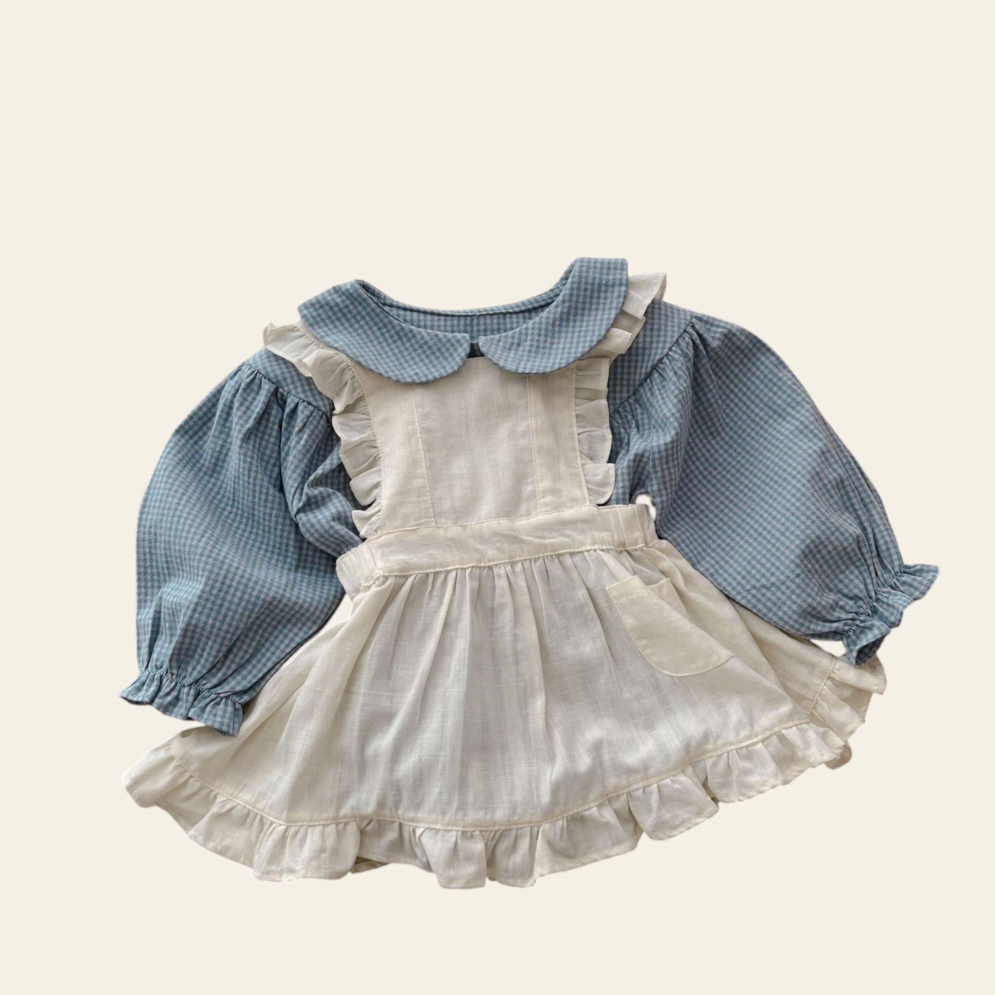 Children's outfit with white dress and blue checkered shirt on a wooden table.