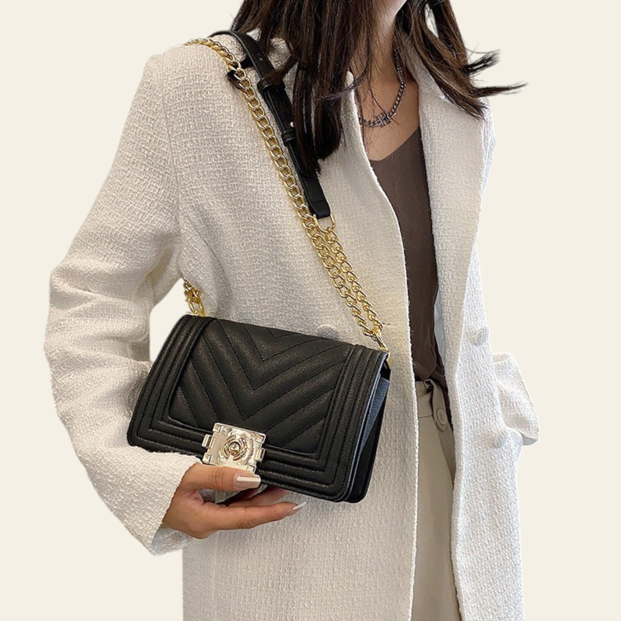 Person holding a black handbag with a gold chain strap in an indoor setting
