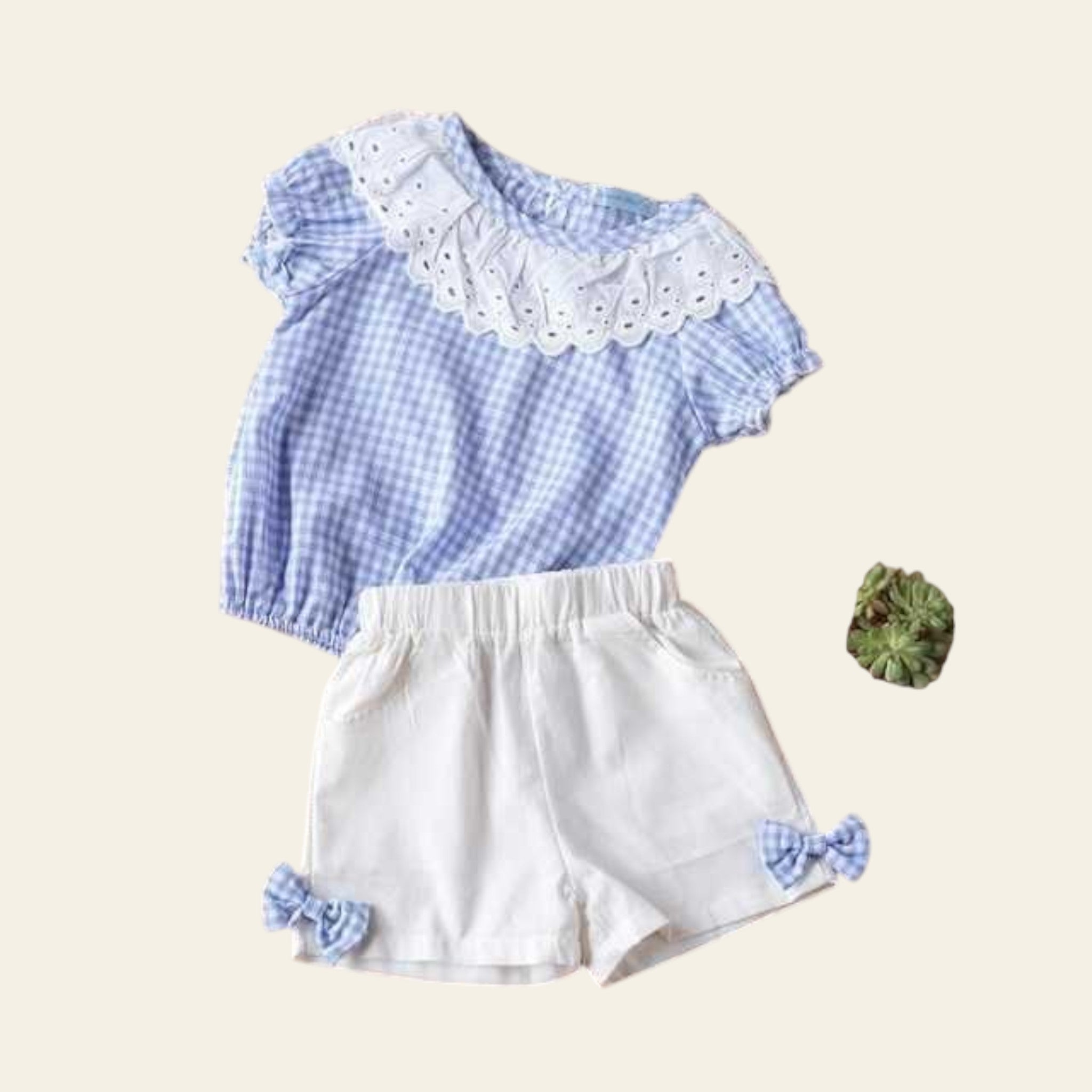 Children's blue checkered top and white shorts on a wooden surface with decorative elements.