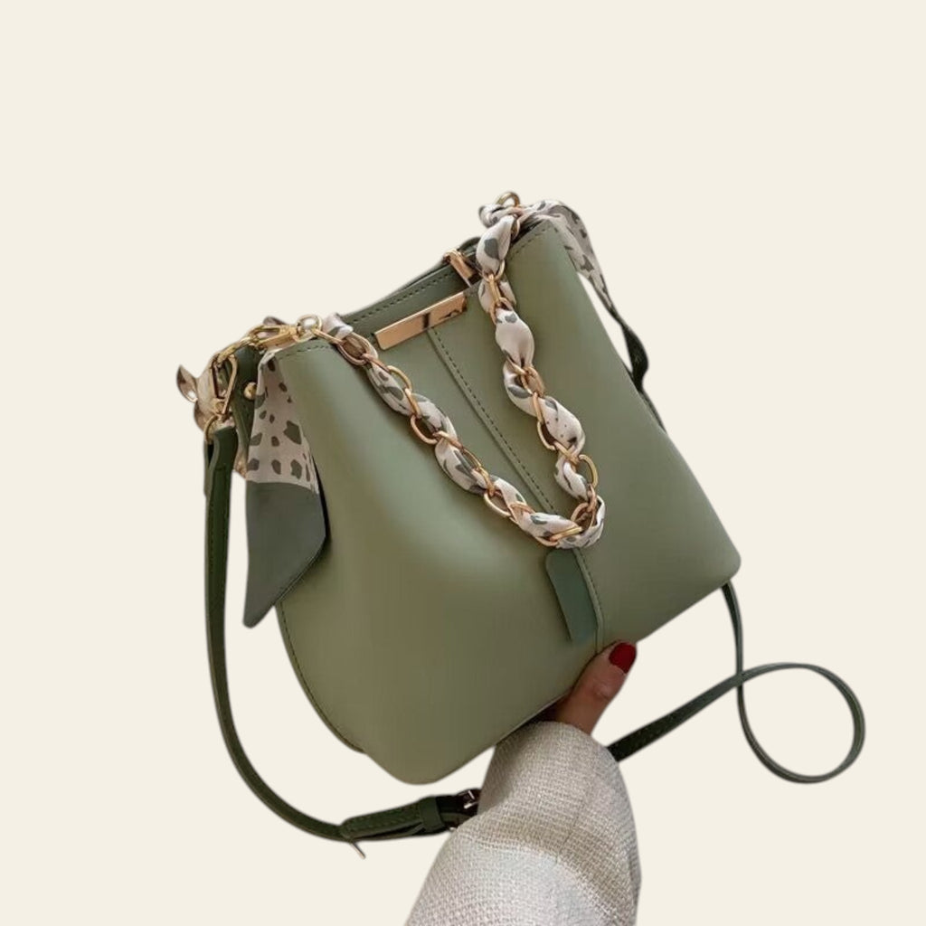 Green handbag with a chain strap held by a hand on a light background