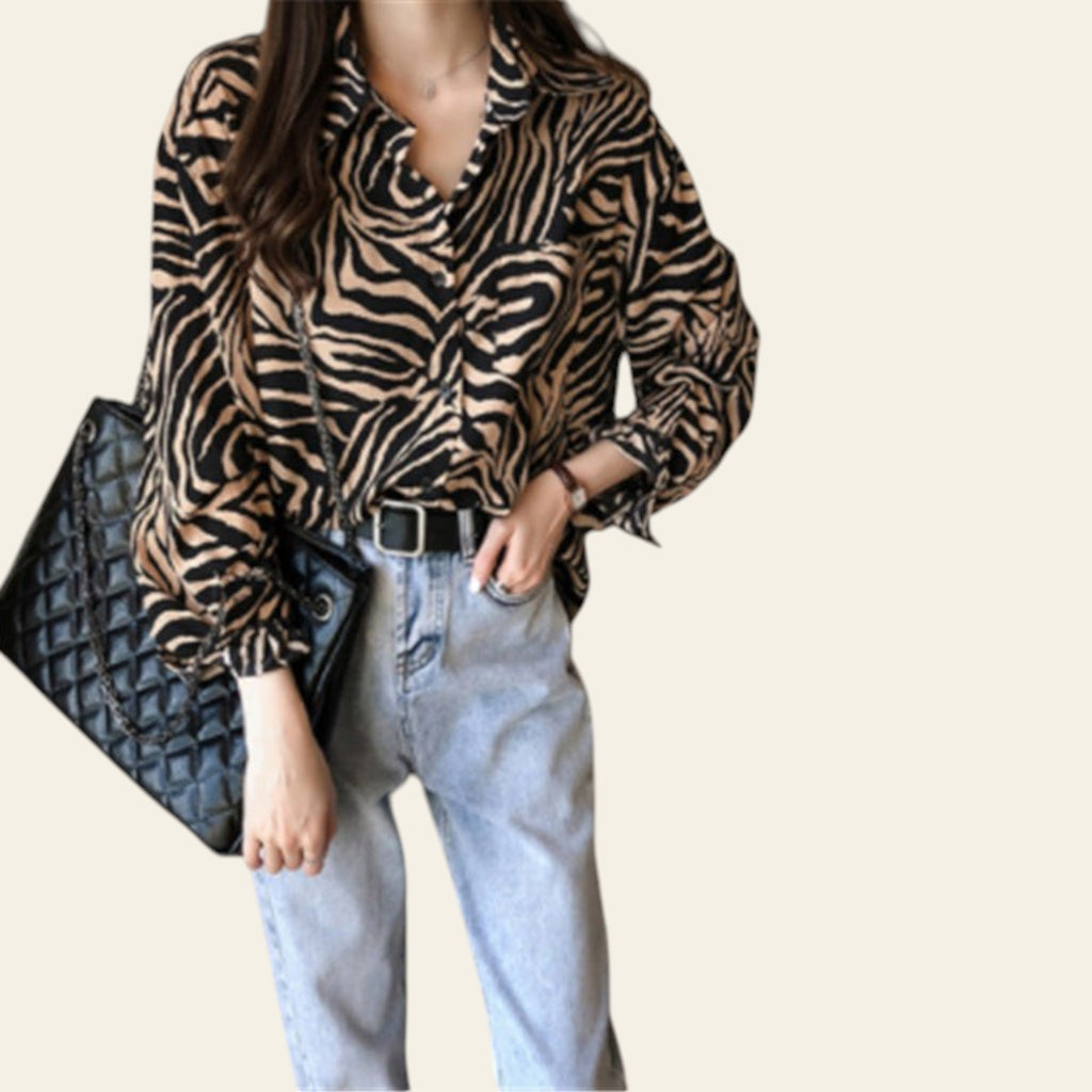 Person wearing a zebra print shirt and light blue jeans, holding a black quilted clutch.