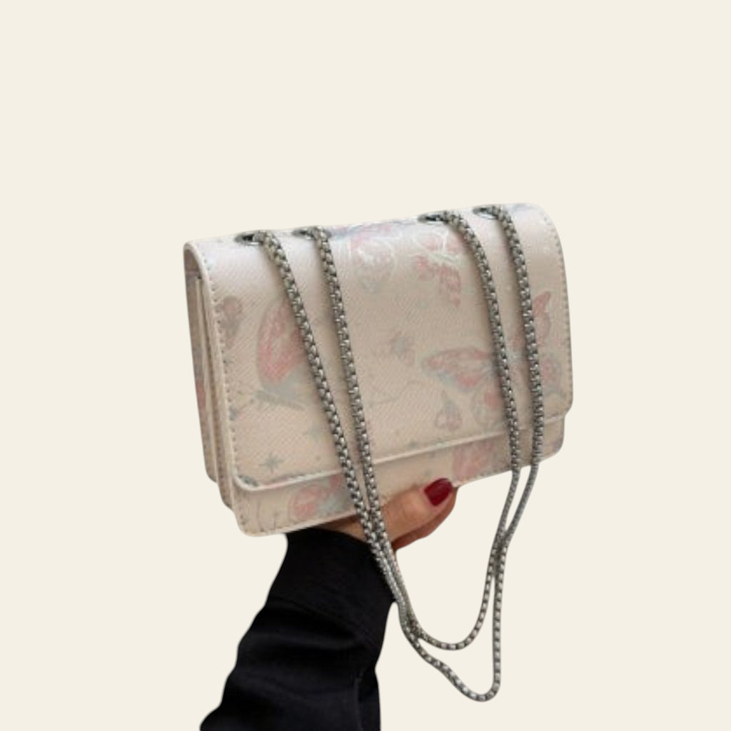 Floral patterned handbag with chain detail held by a person, with a gray coat and book in the background.