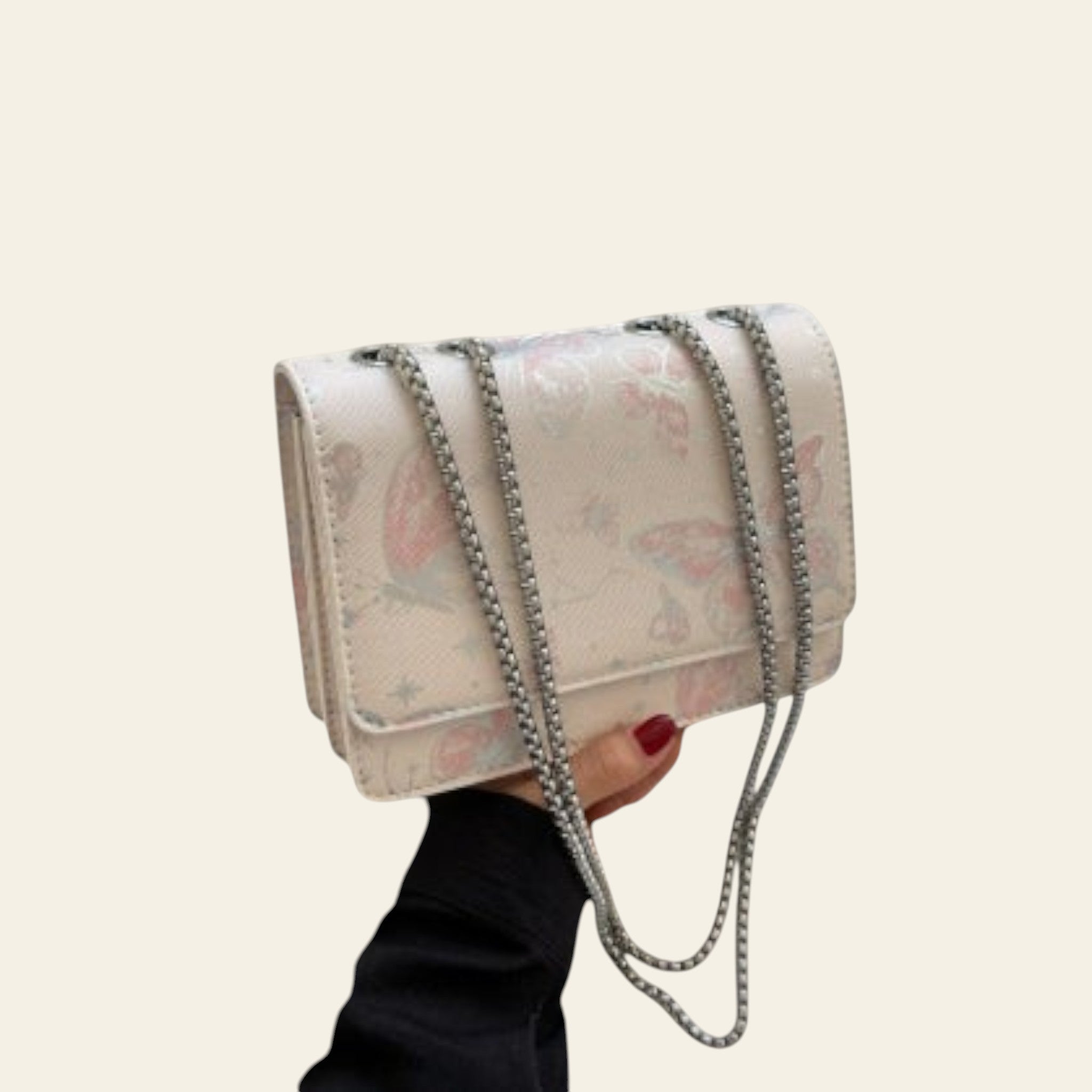 Floral patterned handbag with chain detail held by a person, with a gray coat and book in the background.