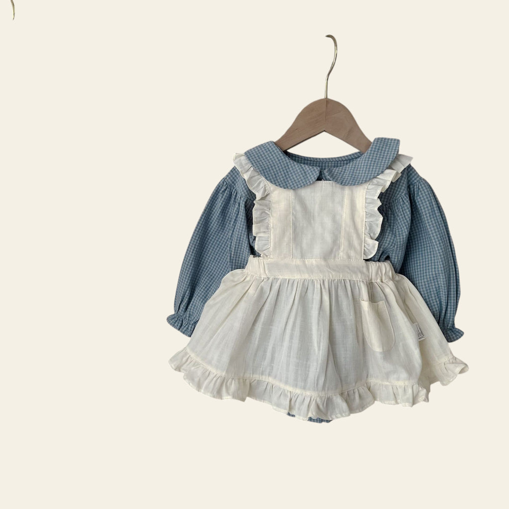 Children's outfit with white dress and blue shirt hanging on a wooden hanger against a neutral background.
