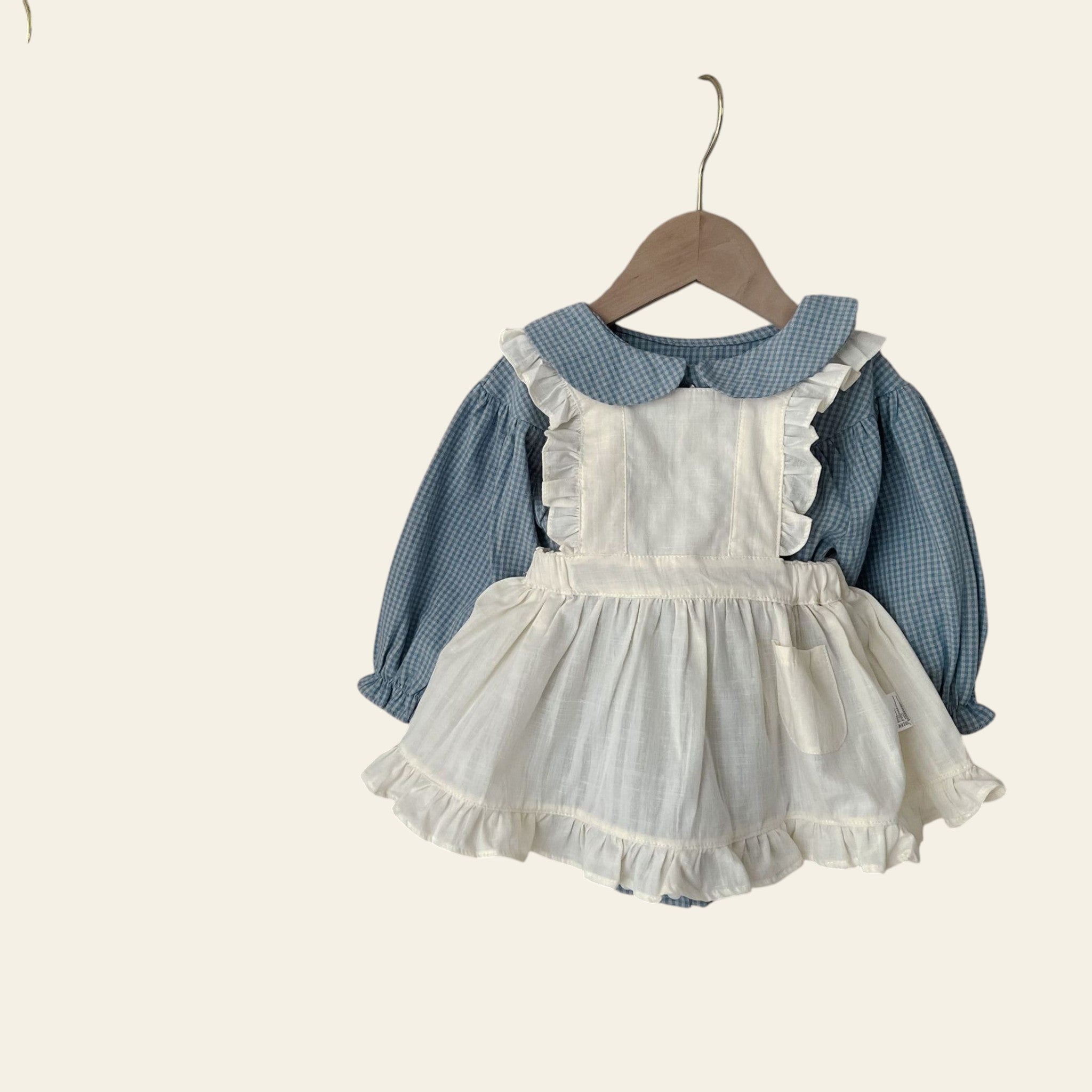 Children's outfit with white dress and blue shirt hanging on a wooden hanger against a neutral background.