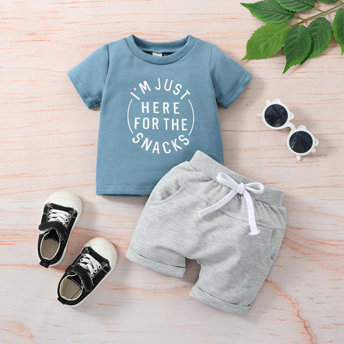 Children's outfit with blue t-shirt, gray shorts, and black shoes on a wooden surface.