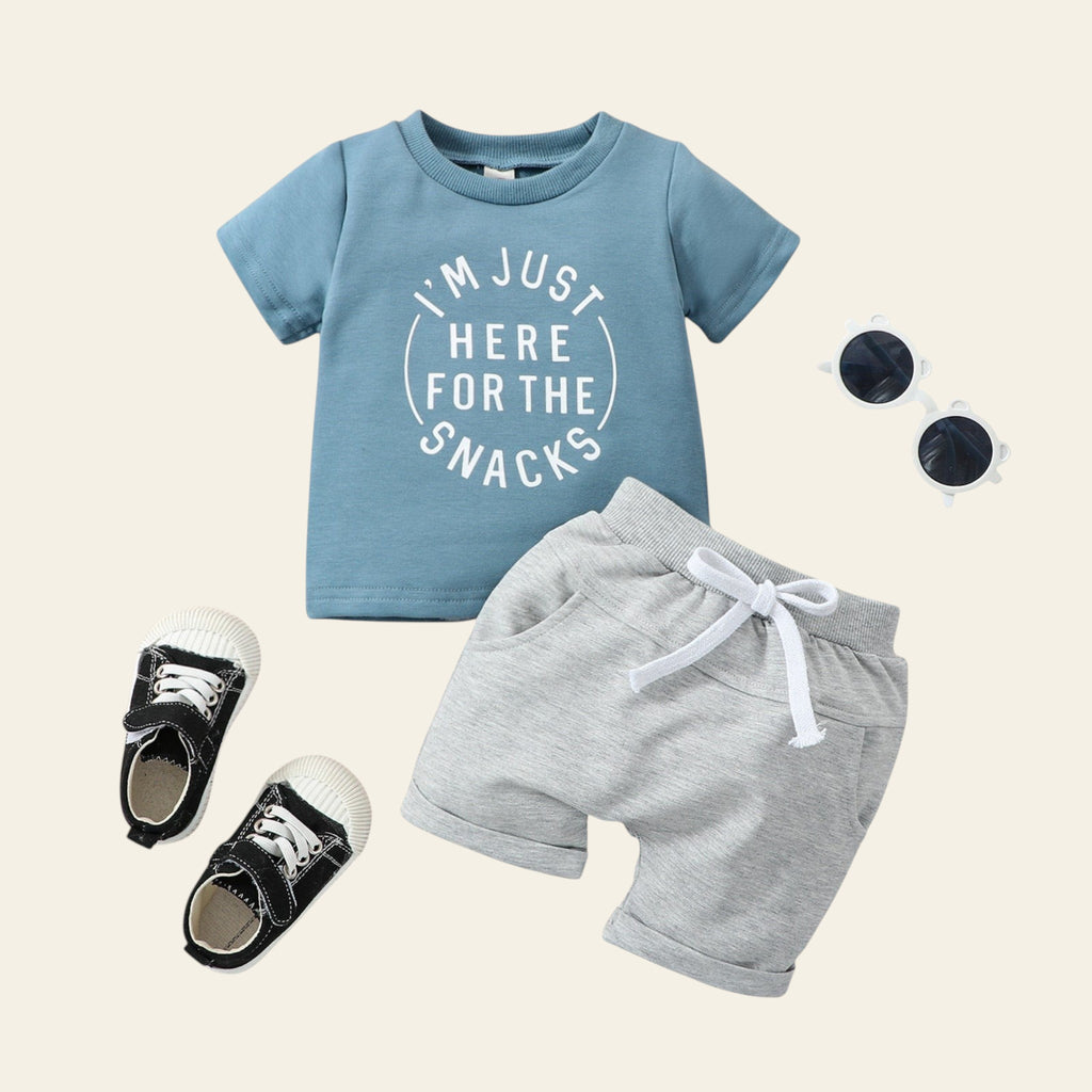 Children's outfit with blue t-shirt, gray shorts, and black shoes on a wooden surface.