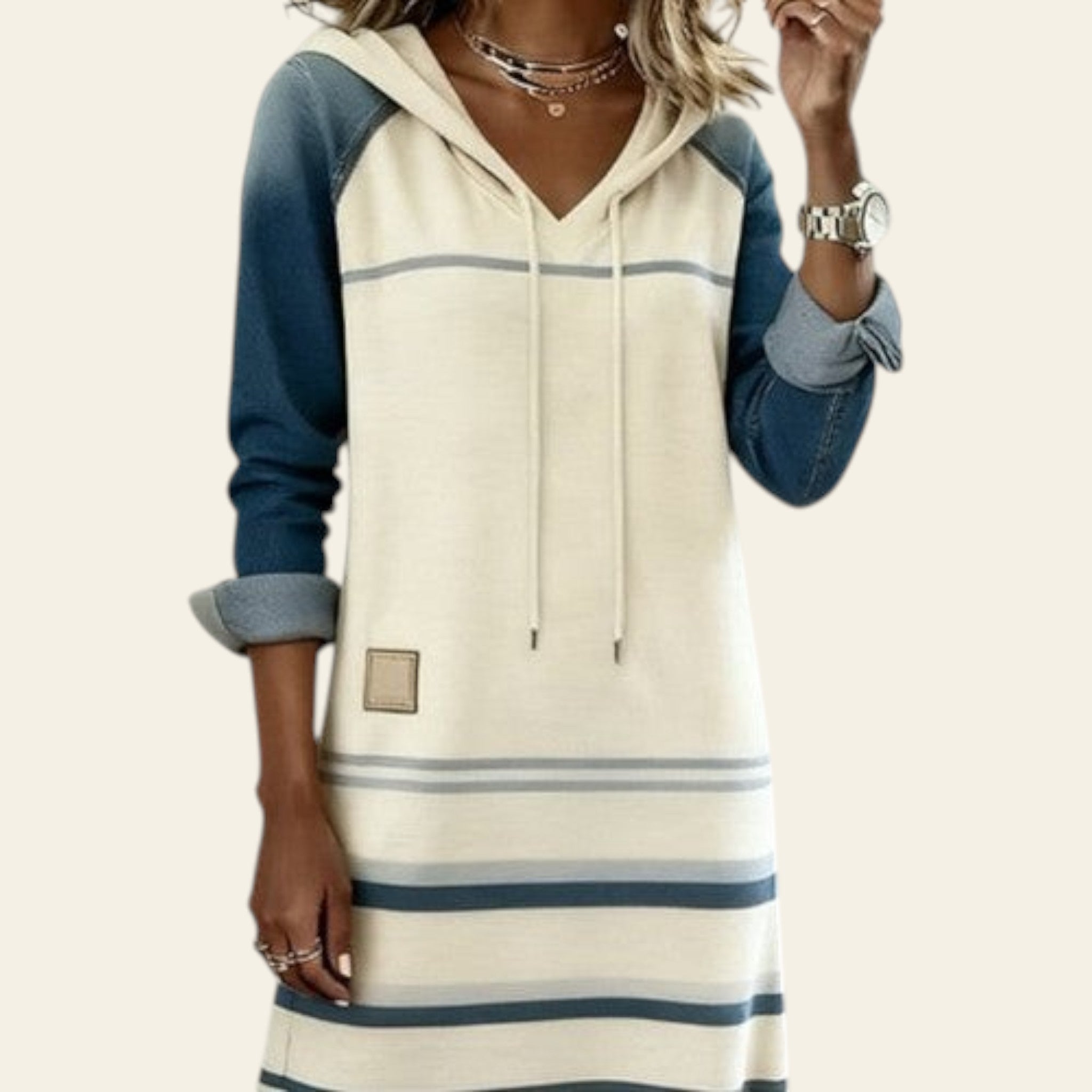 Woman wearing an apricot and blue color-block denim hoodie dress with striped details on a white background