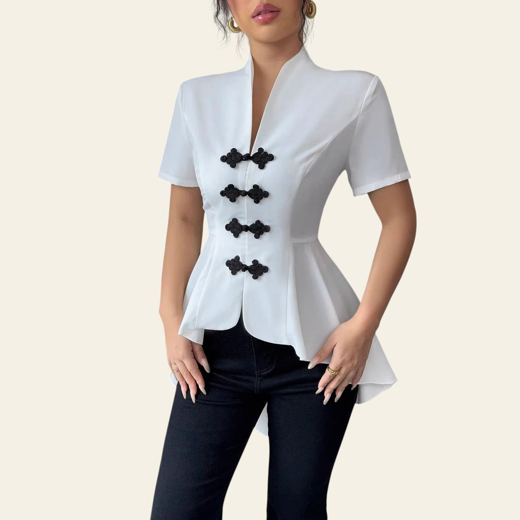 Woman wearing a white blouse with black buttons and black pants in a minimal indoor setting.