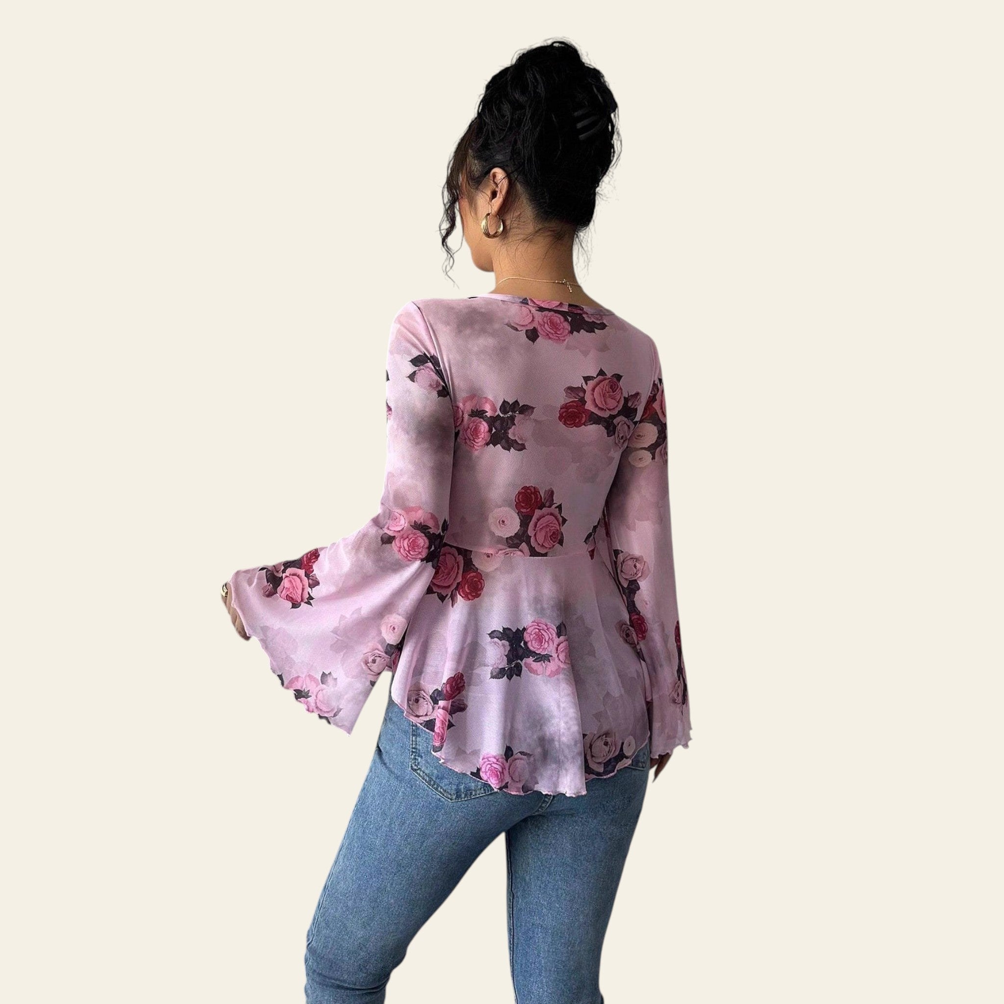 Person wearing a pink floral blouse and blue jeans against a plain background