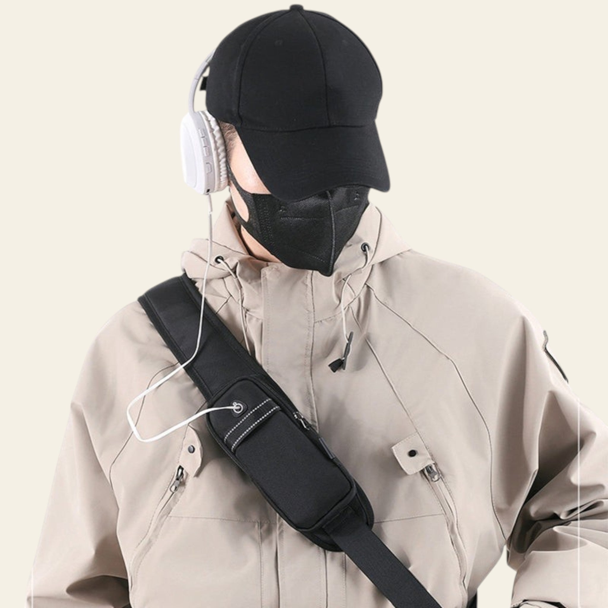 Person wearing a black cap, face mask, and beige jacket with a black shoulder bag on a white background