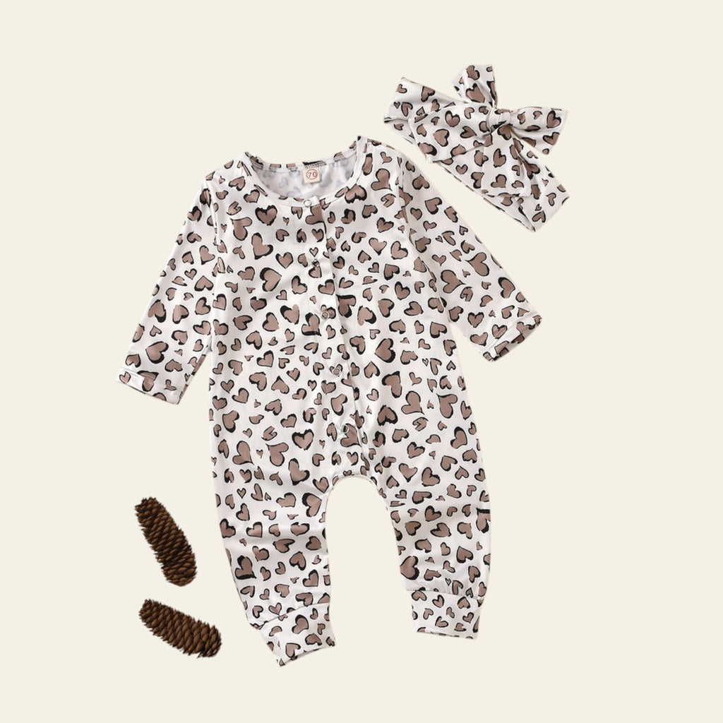 Baby romper with heart pattern, headband, and booties on a beige background