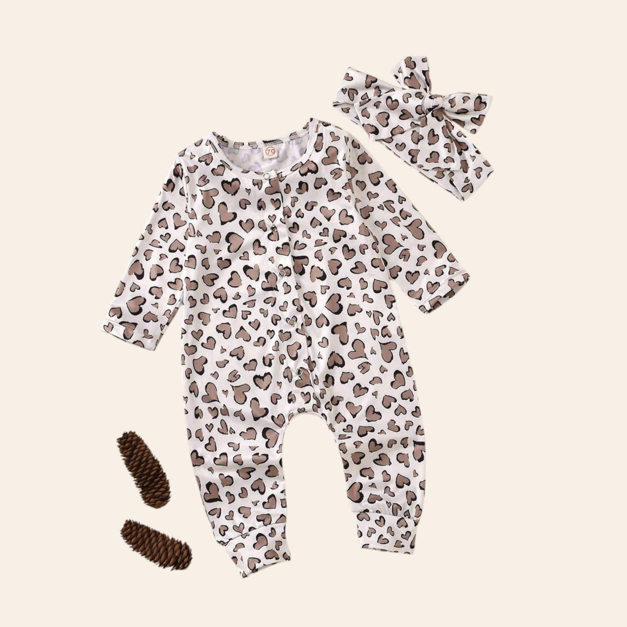 Baby romper with heart pattern, headband, and booties on a beige background