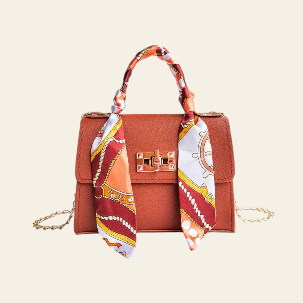 Brown handbag with a colorful scarf draped over it on a light gray background