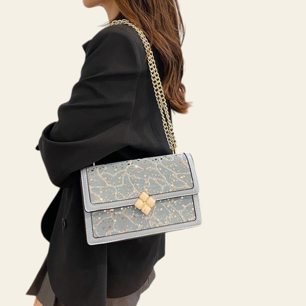 Person holding a light blue handbag with gold chain strap in an indoor setting.