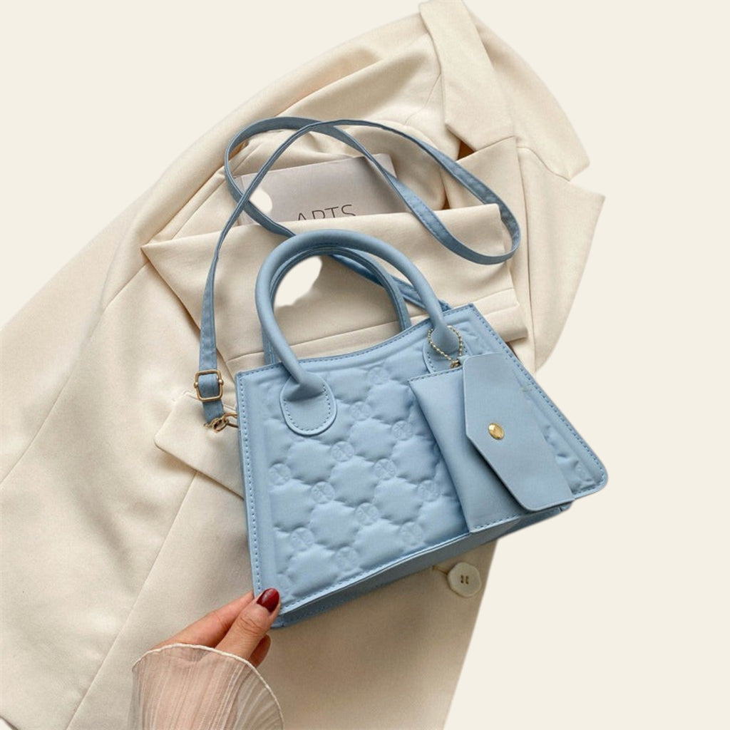 Light blue quilted handbag held by a hand on a beige background