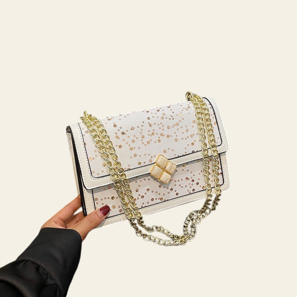 White handbag with gold chain and polka dot pattern on a black surface