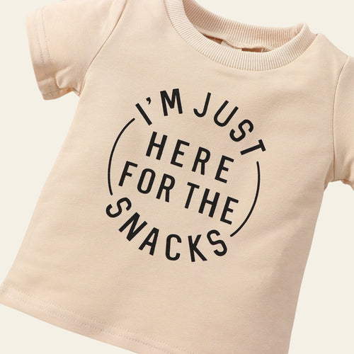 Beige t-shirt with 'I'm just here for the snacks' text on a wooden surface