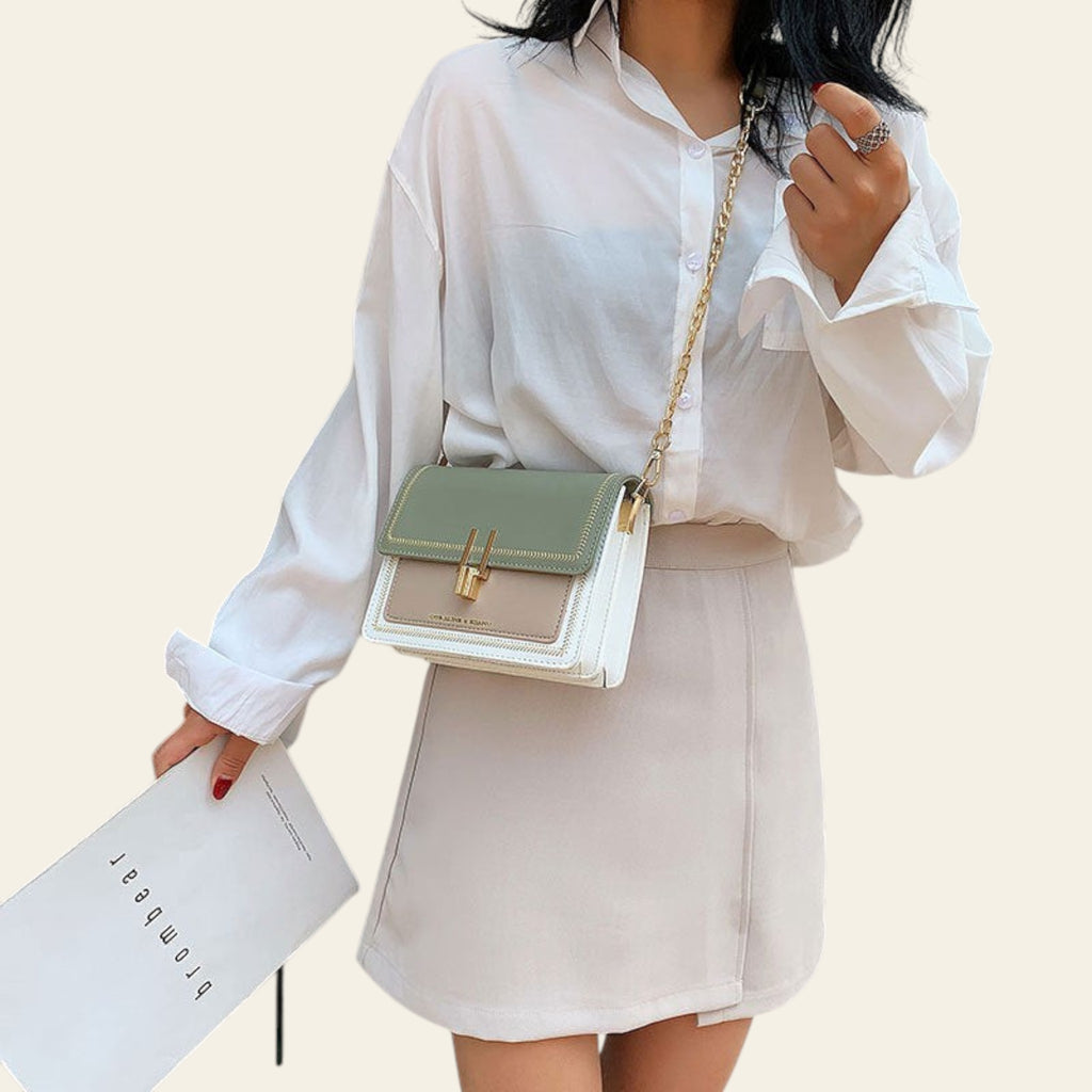 Person wearing a white shirt and holding a green handbag with a neutral bag underneath.