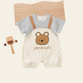 Baby outfit with striped shirt and bear-themed overalls on a white surface